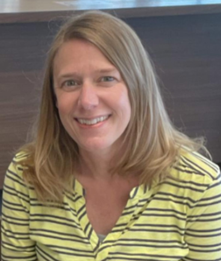 Julie has blondish-brown hair that goes slightly
                below her shoulders. She is wearing a yellow shirt with blue
                double stripes. She is smiling.